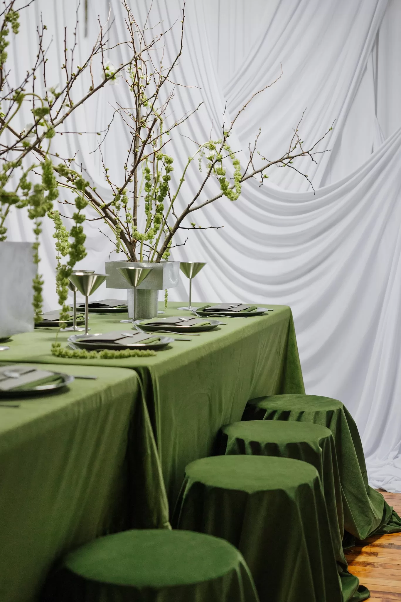 Long reception table with green linens, sculptural branches and modern metallic glassware at Studio Sunset Chicago