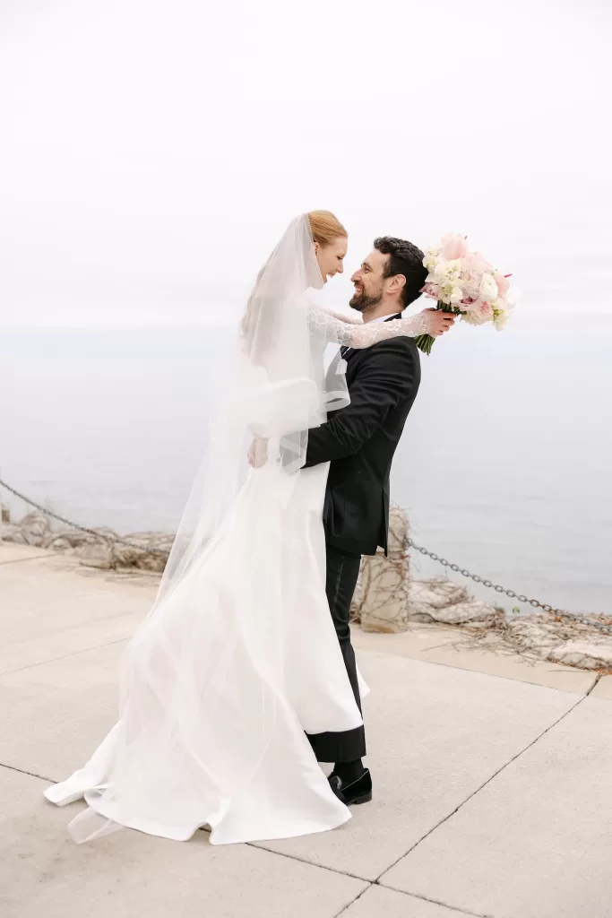 Bride lifted by the groom during a soft waterfront wedding portrait.