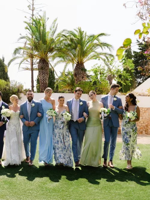 Wedding party walking across the lawn beneath palms in soft blue and green tones.
