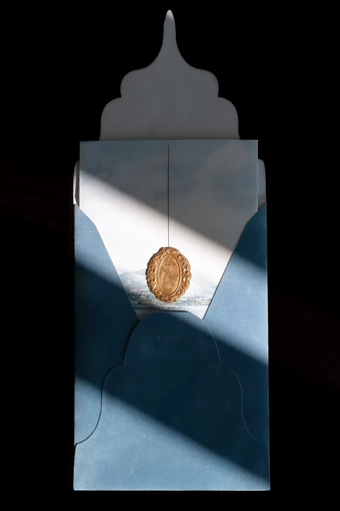 Blue wedding invitation with gold wax seal, caught in a sharp stripe of light.