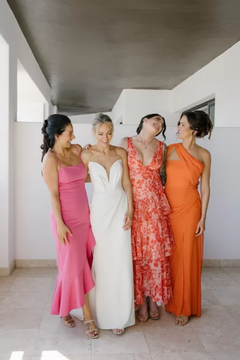 Bride with bridesmaids in pink, coral, and orange dresses before the ceremony.