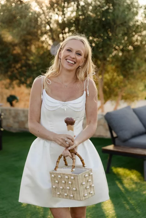 Bride smiling with an ice cream and pearl wicker bag in the late afternoon sun.