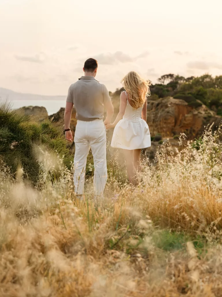 Couple walking through golden coastal grasses near Casa Monte Cristo Collection at sunset.