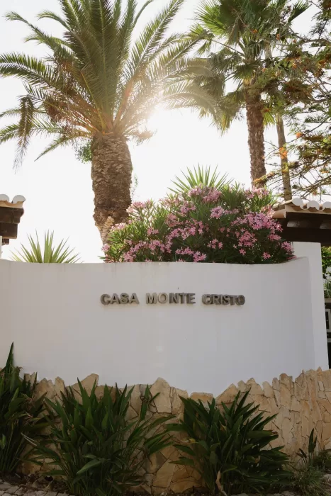 Sunlit Casa Monte Cristo Collection entrance framed by palms and pink flowering shrubs.