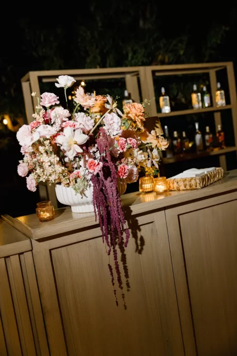 Lush pink and coral flowers styled on a candlelit wooden bar at night.