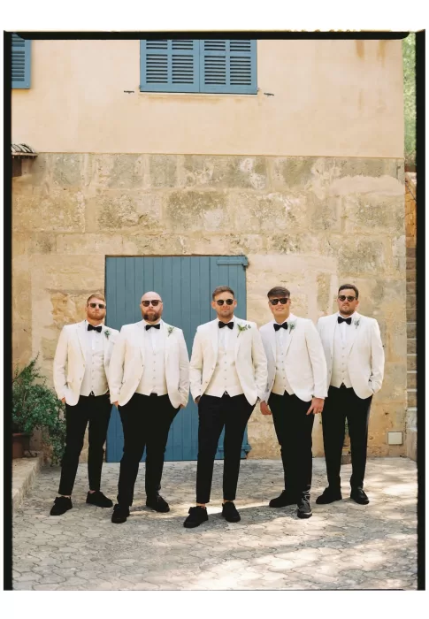 Groomsmen in coordinated suits standing against stone wall, relaxed yet polished group portrait