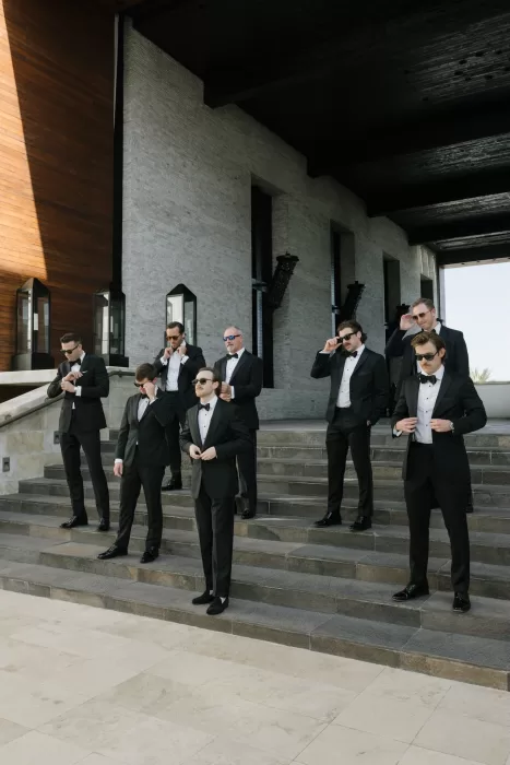 Groomsmen in black tuxedos and sunglasses posed across a modern stone staircase.