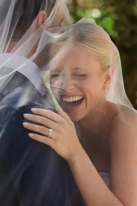Close-up of the bride laughing under her veil during a playful couple portrait.