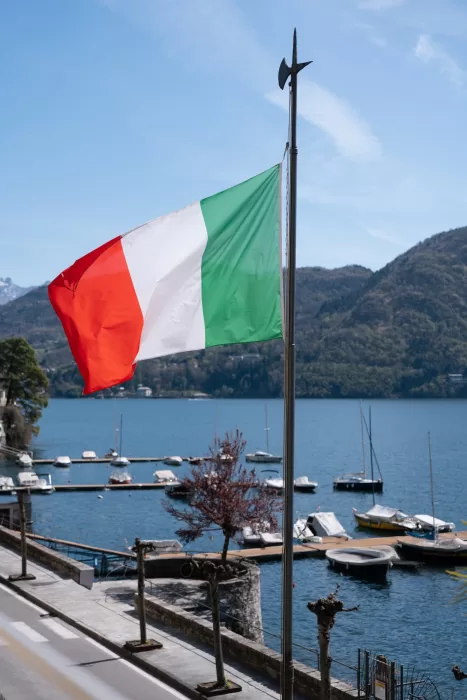 Italian flag flying above Lake Como, with boats and mountains in the distance.