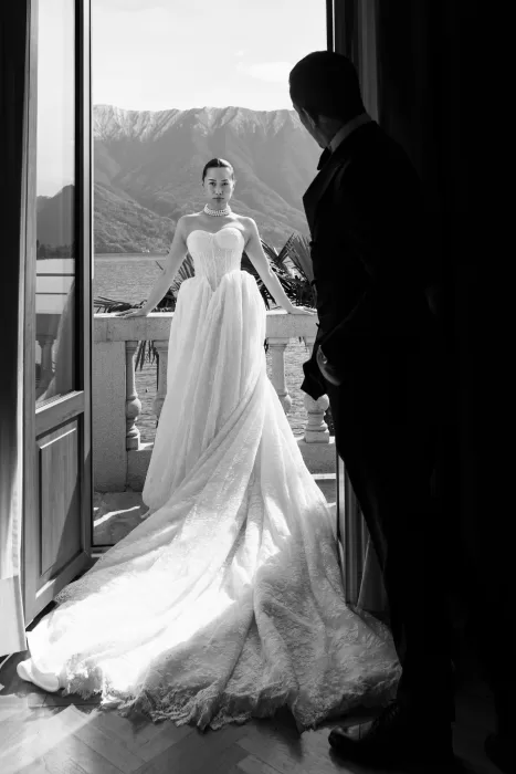 Bride standing on a Lake Como balcony as the groom watches from inside.