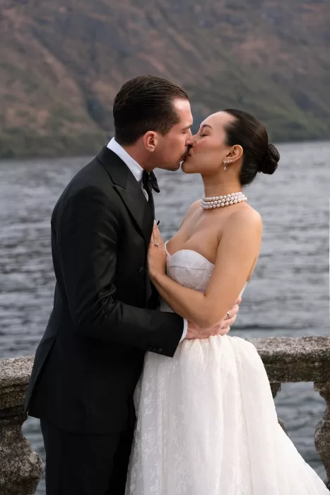 Couple sharing a kiss on a balcony overlooking Lake Como and the mountains.