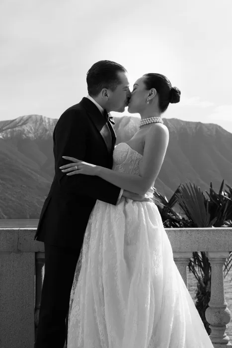 Couple sharing a kiss on a balcony overlooking Lake Como and the mountains.