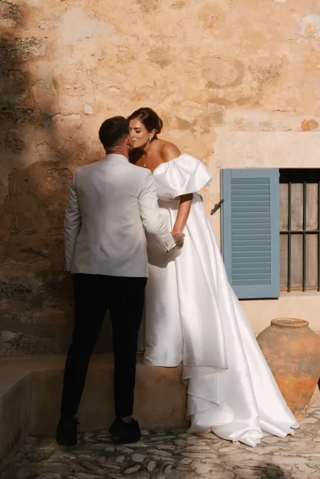 Bride and groom sharing a kiss against a rustic stone wall with blue shutters at a Mallorca finca
