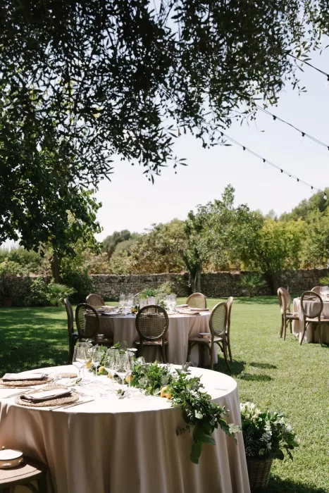 Elegant outdoor reception tables set beneath trees in a Mallorca finca garden with soft sunlight