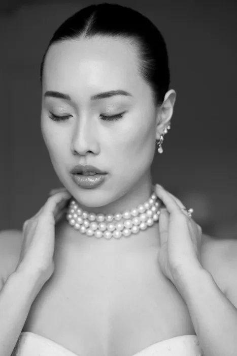 Soft black-and-white bridal portrait with a layered pearl choker and closed eyes.