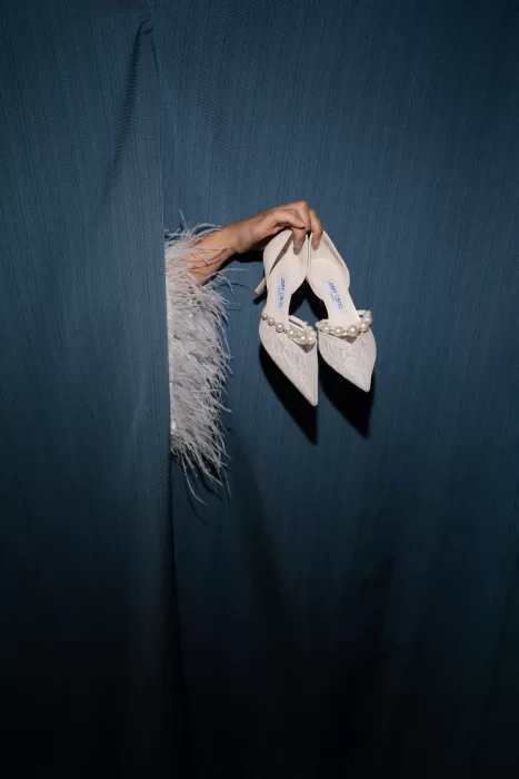 Pearl bridal shoes held through deep blue curtains in a playful fashion detail.