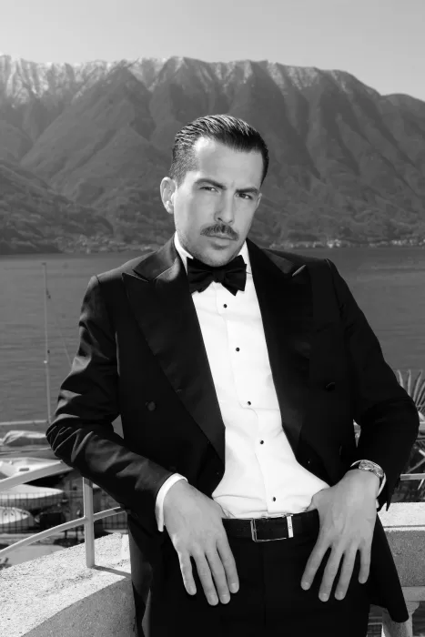 Black-and-white groom portrait in a tuxedo with Lake Como’s mountains behind him.