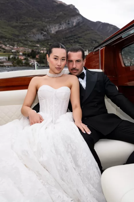 Couple seated together on a classic wooden boat, surrounded by Lake Como scenery.