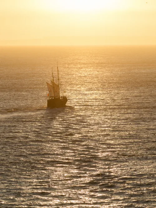 Traditional sailing boat crossing the Algarve coastline at sunset