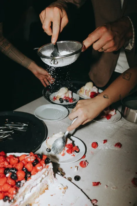 Guests serve berry wedding cake by candlelight, creating a lively late-night dessert moment.