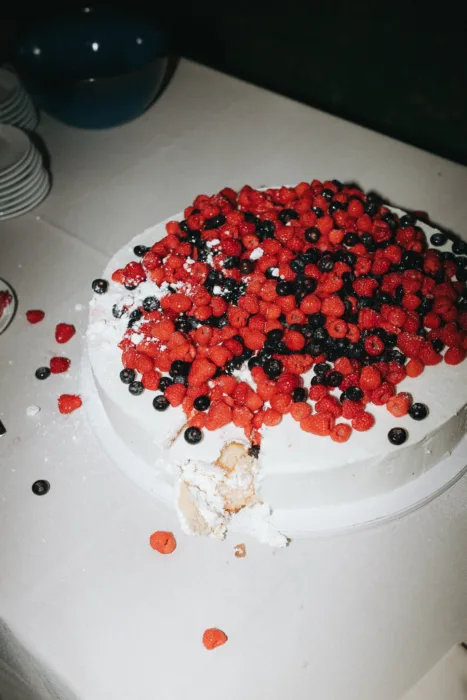 A berry-covered wedding cake sits partly served on a linen-covered reception table.