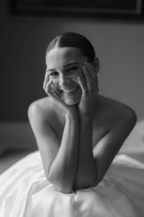 Black and white close-up portrait of a smiling bride resting her face in her hands