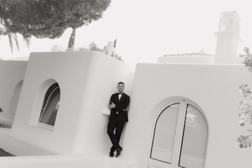 A black and white portrait of the groom against sculptural white villa walls.