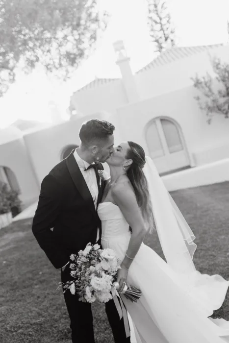 A black and white portrait of the couple kissing in front of the white villa.