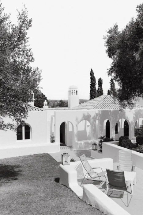 A black and white view of white arched buildings and lounge seating in the sun.