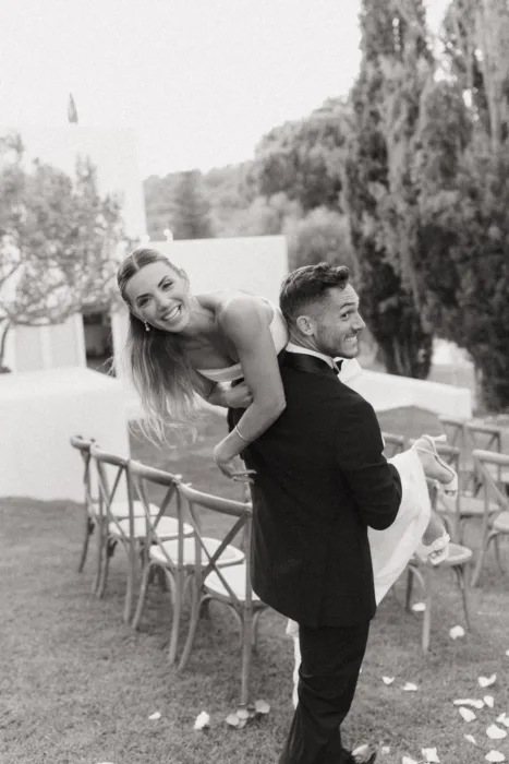 A playful black and white portrait of the couple laughing among ceremony chairs at Casa Arte.