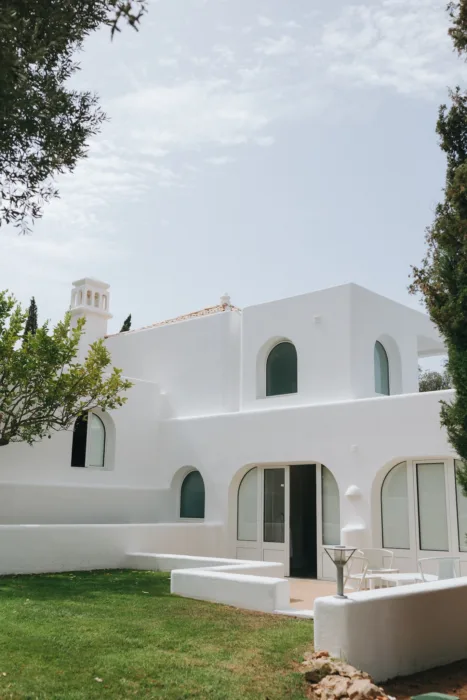 Casa Arte’s white arched villa sits in bright sun, surrounded by lawn and trees.