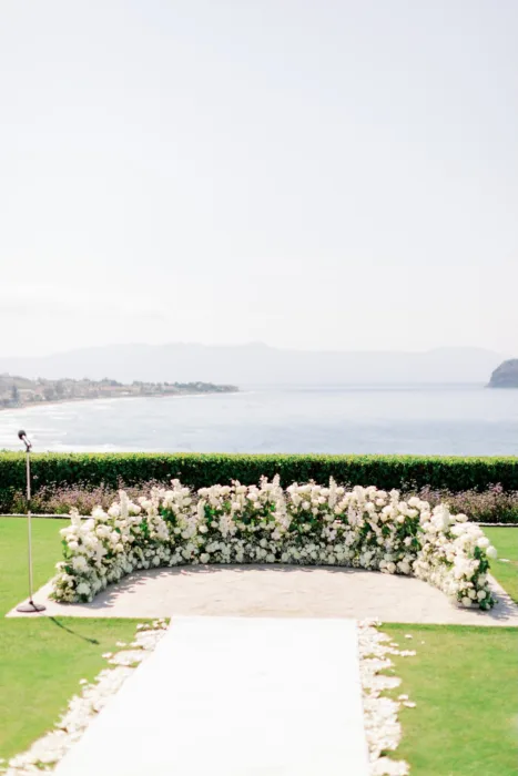White floral ceremony setting overlooking the water and distant coastline.