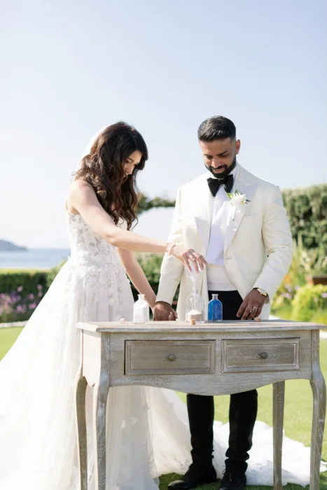 Bride and groom pour sand together during their sunlit outdoor ceremony.