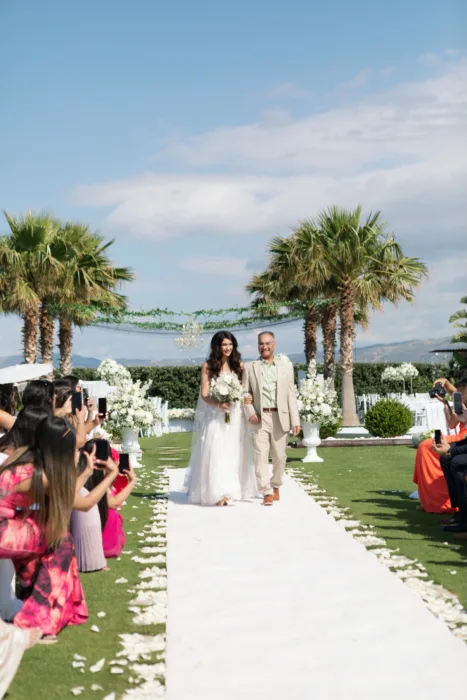 Bride walks down a palm-lined ceremony aisle at Sea View by En Kipo.