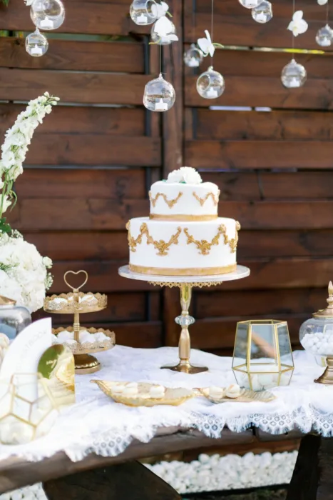 White and gold wedding cake displayed with macarons and hanging glass candles.