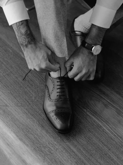 Groom lacing black Oxford wedding shoes during preparations