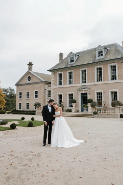 Bride and groom standing in front of Hotham Hall with the country house in the background.