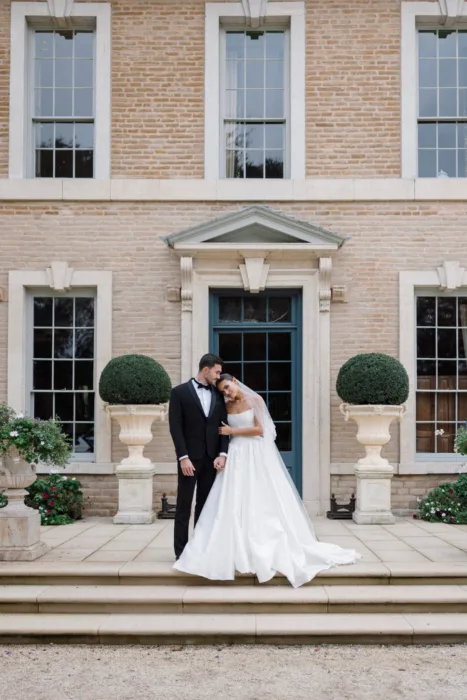 Bride and groom embracing on the front steps of Hotham Hall beneath the main entrance.