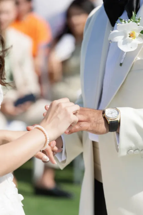 Close-up of the ring exchange with a white orchid boutonniere on the groom’s jacket.