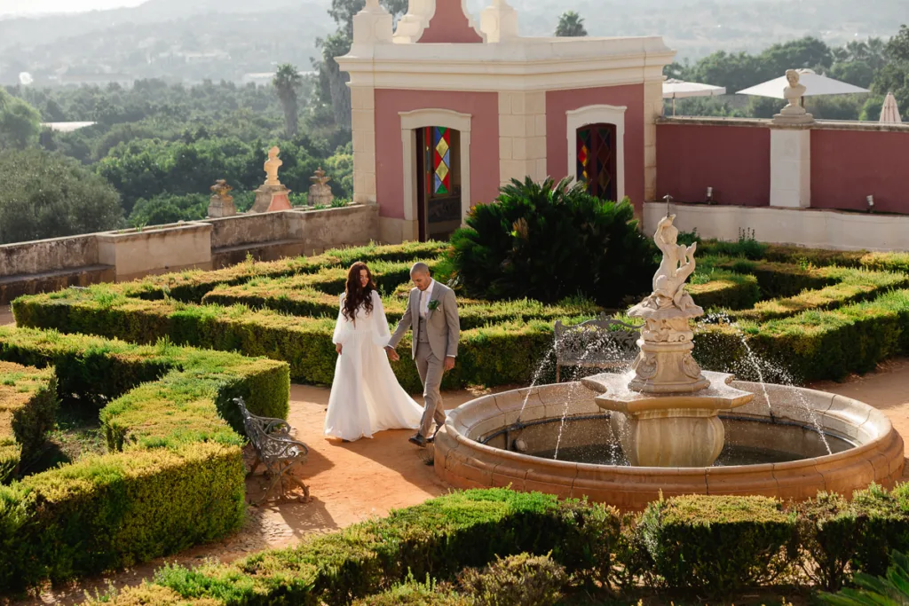 Bride and groom walking through the formal gardens at Pousada Palácio Estoi beside the central fountain