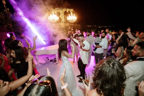 Guests surround the couple on a lively dance floor with purple lighting.