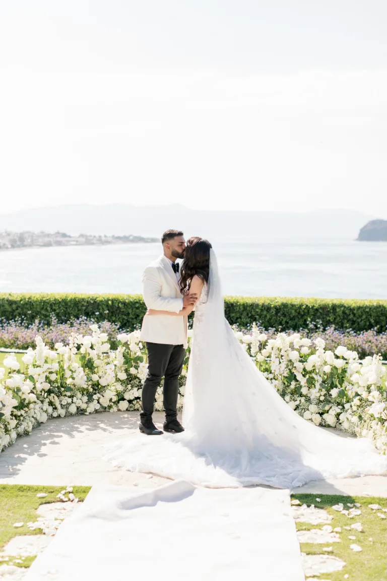 Bride and groom kiss at the floral ceremony space overlooking the water.