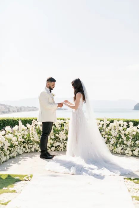 Couple exchange rings at Sea View by En Kipo with the coastline behind them.