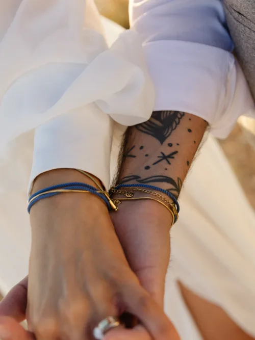 Close-up of the bride and groom holding hands showing bracelets, wedding rings and a tattoo