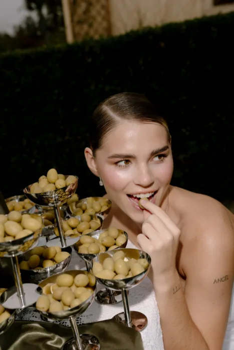 Close-up of the bride biting into a green olive, silver coupes stacked in the foreground