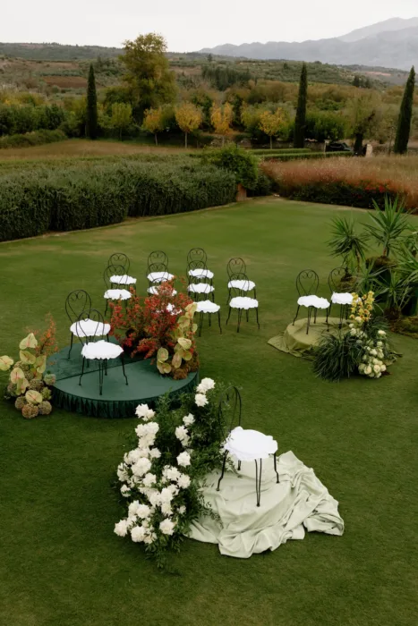 Clusters of ceremony chairs on velvet-green platforms, with cypress trees and mountains rising beyond