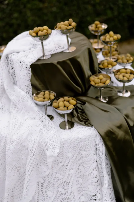 Close-up of green olives piled in silver coupes, set on crochet lace and draped satin