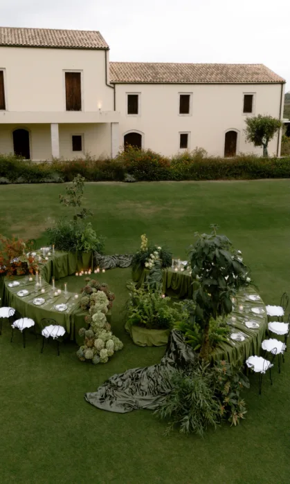 Spiral dinner table dressed in moss-green linen on the lawn in front of the Roxani Estate farmhouse