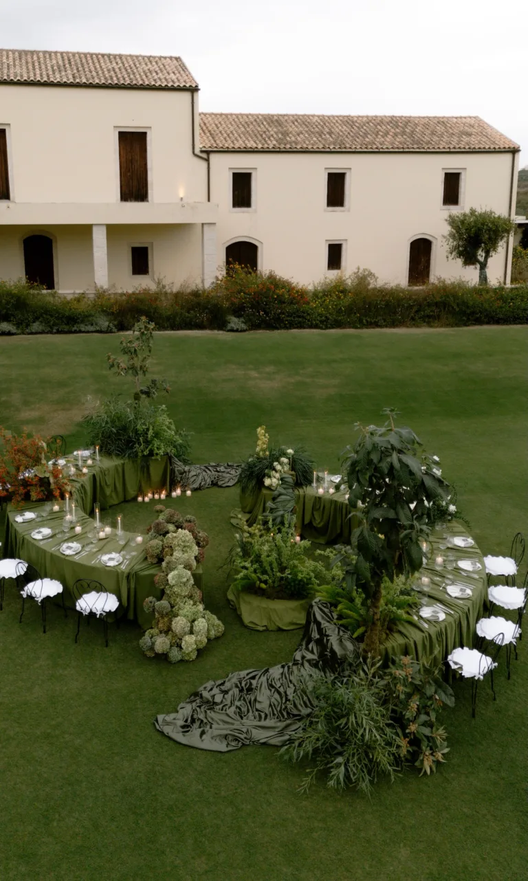 Spiral dinner table dressed in moss-green linen on the lawn in front of the Roxani Estate farmhouse