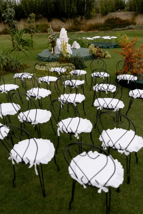 Rows of black wrought-iron chairs with ruffled white cushions set across the lawn for a garden ceremony